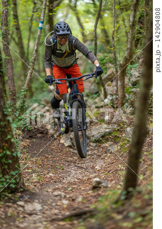 Mountain biking cyclist riding a trail through a rocky forest wearing helmet and hydration pack Mountain biking cyclist riding a trail through a rocky forest wearing helmet and hydration pack 142904808