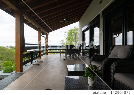 Spacious covered patio terrace with wicker seating, dining table and scenic countryside view Spacious covered patio terrace with wicker seating, dining table and scenic countryside view 142904873