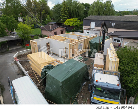 Construction site showing timber frame house assembly with crane, truck and stacked panels in residential area 142904945