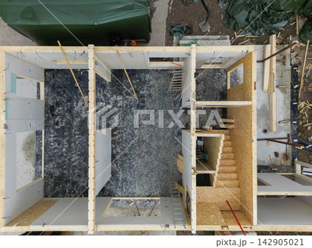Aerial top view of wooden house construction showing framing, stairs and interior layout under construction Aerial top view of wooden house construction showing framing, stairs and interior layout under construction 142905021