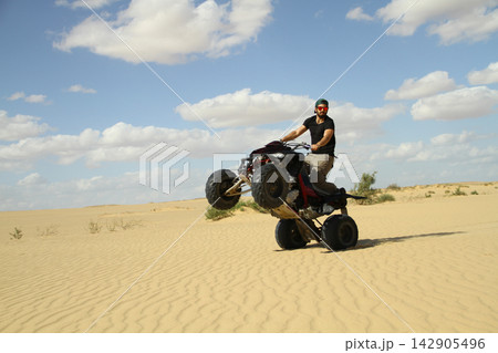 Young quad bike rider doing wheelie in desert 142905496