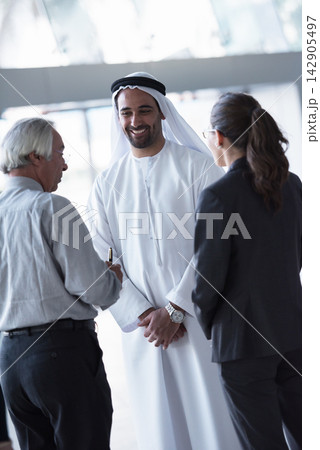 Emirati businessman in traditional kandura smiling while talking with colleagues during a professional meeting 142905497