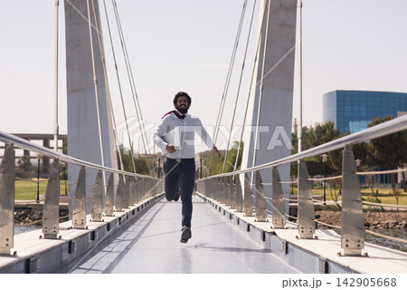 Businessman running across pedestrian bridge with laptop, hurrying to work on a sunny day 142905668