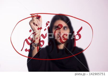 Woman writing Arabic New Year greeting on glass with red marker in festive calligraphy 142905751
