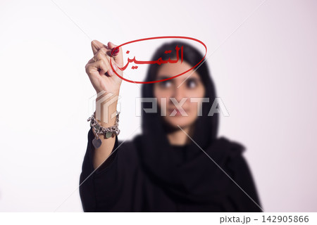 Arabic woman writing 'excellence' on glass with red marker to highlight achievement and business leadership Arabic woman writing 'excellence' on glass with red marker to highlight achievement and business leadership 142905866