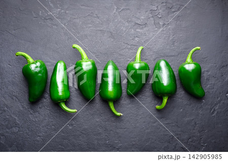 Small jalapeno peppers aligned in row on dark stone surface Small jalapeno peppers aligned in row on dark stone surface 142905985