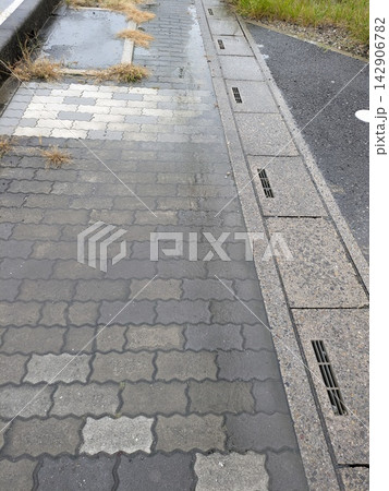 雨で濡れた歩道と道路脇に並ぶ雨水排水口 雨で濡れた歩道と道路脇に並ぶ雨水排水口 142906782
