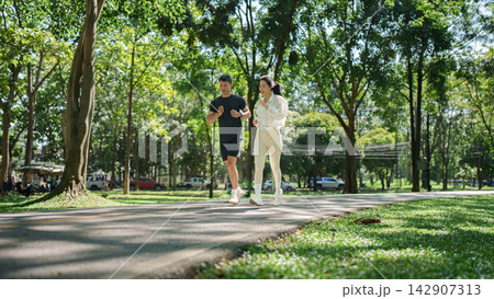 Asian couple jogging along park path for outdoor fitness and healthy lifestyle 142907313