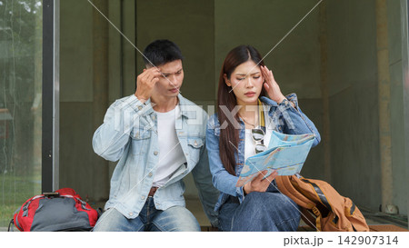 Asian tourist couple looking at map with stressed confused expression while lost on trip Asian tourist couple looking at map with stressed confused expression while lost on trip 142907314