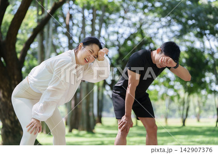 Exhausted Asian couple wiping sweat after outdoor workout for endurance fitness Exhausted Asian couple wiping sweat after outdoor workout for endurance fitness 142907376