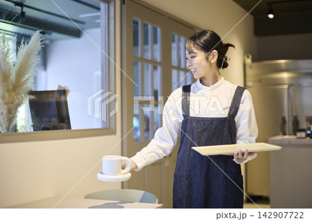 カフェのテーブルにコーヒーを運ぶ女性スタッフ カフェのテーブルにコーヒーを運ぶ女性スタッフ 142907722