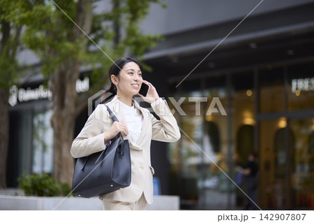 オフィス街を歩きながらスマートフォンで通話する女性 オフィス街を歩きながらスマートフォンで通話する女性 142907807