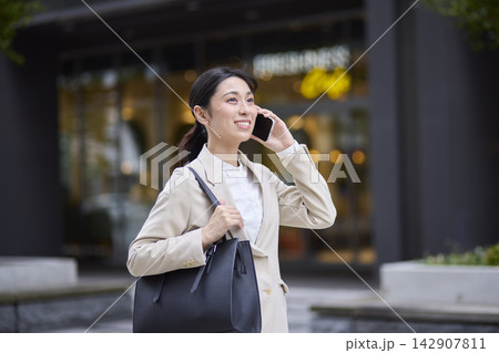 オフィス街を歩きながらスマートフォンで通話する女性 オフィス街を歩きながらスマートフォンで通話する女性 142907811