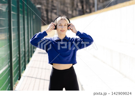 Young sportswoman adjusting headphones before training outdoors Young sportswoman adjusting headphones before training outdoors 142909024