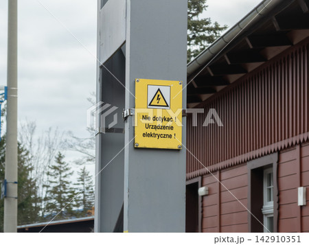 A bright yellow caution sign attached to a metal utility pole warns people of electrical equipment, emphasizing public safety, hazard awareness, and industrial zone danger protection 142910351