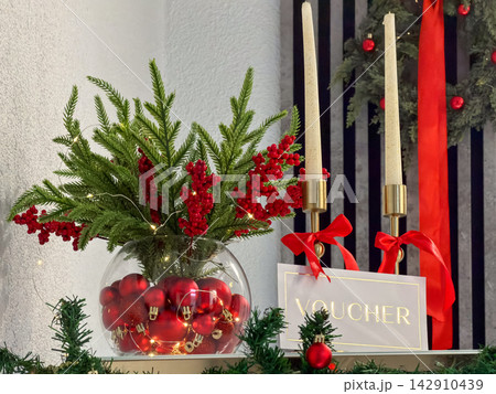 A holiday festive centerpiece featuring red ornaments in a glass bowl with evergreen branches and candles, creating a warm elegant atmosphere for seasonal gift voucher marketing A holiday festive centerpiece featuring red ornaments in a glass bowl with evergreen branches and candles, creating a warm elegant atmosphere for seasonal gift voucher marketing 142910439