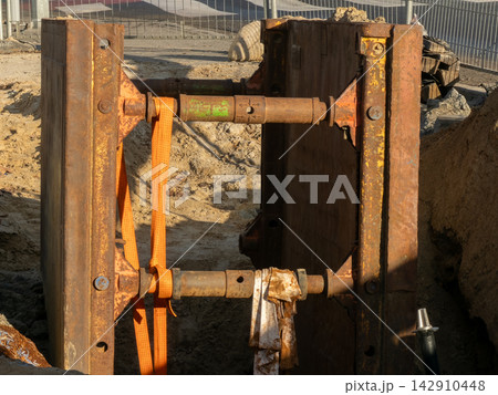 Heavy steel trench box for site shoring in a deep excavation, securing construction workers and infrastructure against soil collapse at a busy urban development project during daylight Heavy steel trench box for site shoring in a deep excavation, securing construction workers and infrastructure against soil collapse at a busy urban development project during daylight 142910448