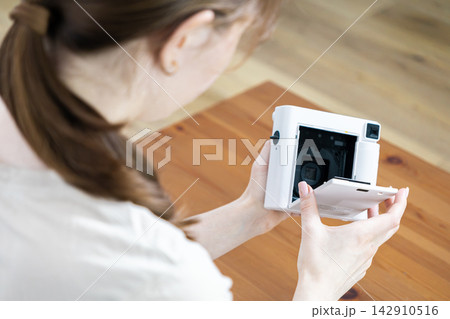 A young person loads instant film into a modern white camera, creating a nostalgic memory capturing experience in a bright home setting with a focus on hobbyist artistic photography 142910516