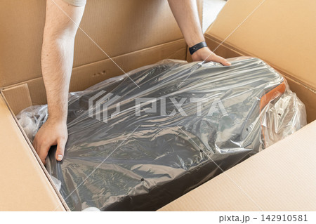 Person unpacking a new gaming chair from a large cardboard box, representing home delivery, online shopping, furniture assembly, and the excitement of setting up a workspace indoors Person unpacking a new gaming chair from a large cardboard box, representing home delivery, online shopping, furniture assembly, and the excitement of setting up a workspace indoors 142910581