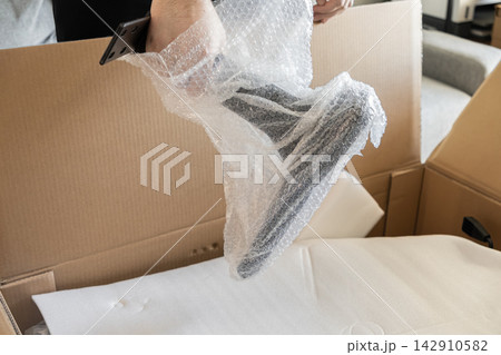 A hand carefully unwraps a black metal furniture leg from protective bubble wrap inside a large cardboard shipping box, capturing the excitement of assembling new home decor items A hand carefully unwraps a black metal furniture leg from protective bubble wrap inside a large cardboard shipping box, capturing the excitement of assembling new home decor items 142910582