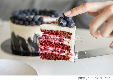 A person lifts a slice of gourmet red velvet berry cake with a silver server from a whole dessert, highlighting culinary craft and indulgence in a bright modern kitchen restaurant 142910602
