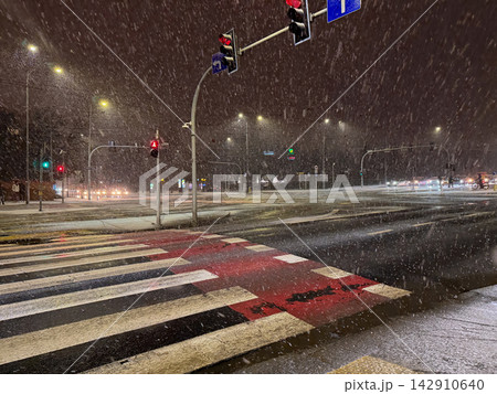 A snowy urban intersection at night with glowing traffic lights and illuminated street signs, capturing a cold atmospheric cityscape during a winter storm in a bustling city center A snowy urban intersection at night with glowing traffic lights and illuminated street signs, capturing a cold atmospheric cityscape during a winter storm in a bustling city center 142910640