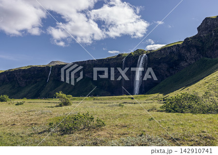 Seljalandsfoss waterfall in Iceland with grassy foreground and blue summer sky Seljalandsfoss waterfall in Iceland with grassy foreground and blue summer sky 142910741
