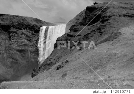 Black and white Skogafoss waterfall with grassy slopes in southern Iceland 142910771