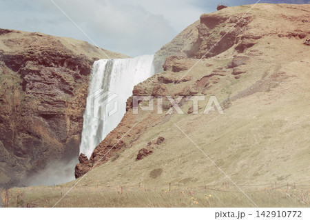Skogafoss waterfall and steep grassy cliffs in a muted summer Iceland landscape 142910772