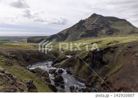 Skoga River Rapids and Grassy Gorge Beneath a Steep Mountain in Iceland Skoga River Rapids and Grassy Gorge Beneath a Steep Mountain in Iceland 142910807