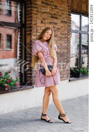 Joyful woman in pink summer dress reaching forward on city street Joyful woman in pink summer dress reaching forward on city street 142911004