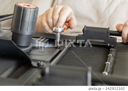 A person uses a metal ratchet tool to tighten a bolt on a black office chair mechanism, representing professional furniture assembly or DIY home repair project in a work environment A person uses a metal ratchet tool to tighten a bolt on a black office chair mechanism, representing professional furniture assembly or DIY home repair project in a work environment 142912102