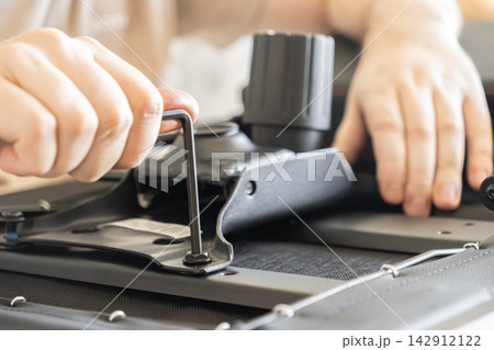 A person tightens a bolt with an allen key while assembling a modern office chair at home, representing DIY furniture construction, home improvement, and manual technical assembly tasks 142912122