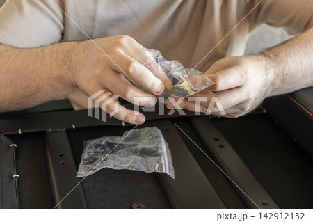 Hands holding a clear plastic bag containing adhesive felt furniture pads over a metal chair frame, representing the careful assembly process of modern home office seating furniture Hands holding a clear plastic bag containing adhesive felt furniture pads over a metal chair frame, representing the careful assembly process of modern home office seating furniture 142912132