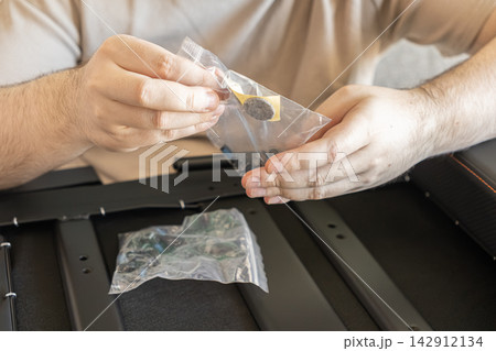 A person holds a small plastic bag with furniture assembly parts while building a metal frame, illustrating home improvement, DIY repair work, and the process of construction tasks A person holds a small plastic bag with furniture assembly parts while building a metal frame, illustrating home improvement, DIY repair work, and the process of construction tasks 142912134