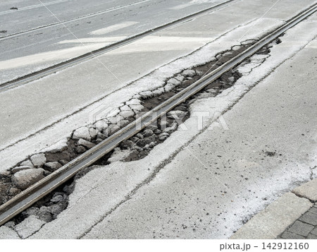 A damaged tram track embedded in broken asphalt road pavement shows crumbling concrete and debris along the rail, highlighting urban decay, infrastructure neglect and hazardous transit 142912160