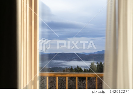 A view of pine forest mountains and morning mist through a bedroom window, conveying tranquil solitude, natural beauty, and a cozy escape in a quiet mountain cabin resort stay 142912274