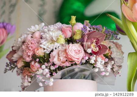 A lush bouquet of pink roses, white chrysanthemums, and orchids in a rounded box serves as an elegant floral arrangement for celebratory occasions, weddings, or birthday gifts 142912289
