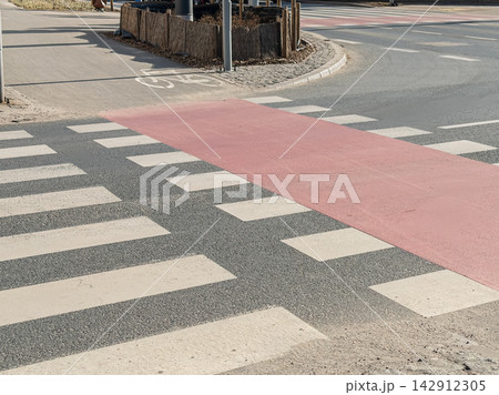 A marked crosswalk featuring red bicycle lane surfacing at a sunny city intersection, highlighting urban infrastructure design aimed at enhancing pedestrian safety and traffic flow A marked crosswalk featuring red bicycle lane surfacing at a sunny city intersection, highlighting urban infrastructure design aimed at enhancing pedestrian safety and traffic flow 142912305