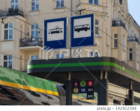 A public transport stop sign featuring symbols for trams and buses with route numbers standing against a classic European city building for urban commuting and city mobility travel A public transport stop sign featuring symbols for trams and buses with route numbers standing against a classic European city building for urban commuting and city mobility travel 142912308