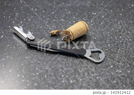 A broken wine cork rests beside a black pocket corkscrew opener on a granite kitchen surface, depicting the frustration of opening a bottle with a damaged closure for evening dining A broken wine cork rests beside a black pocket corkscrew opener on a granite kitchen surface, depicting the frustration of opening a bottle with a damaged closure for evening dining 142912412