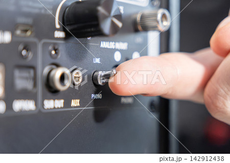 A finger flipping a phono line toggle switch on a black audio amplifier back panel, representing manual configuration of high fidelity stereo hardware for music sound system setup A finger flipping a phono line toggle switch on a black audio amplifier back panel, representing manual configuration of high fidelity stereo hardware for music sound system setup 142912438