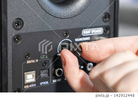 A hand adjusts the volume knob on a professional studio speaker to change audio output levels for a high quality sound experience in a modern music production or home entertainment studio A hand adjusts the volume knob on a professional studio speaker to change audio output levels for a high quality sound experience in a modern music production or home entertainment studio 142912448