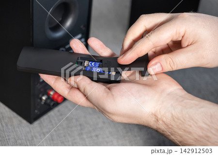 A person replaces batteries in a black remote control to restore device functionality, showcasing a routine home maintenance task and troubleshooting of electronics in a living area A person replaces batteries in a black remote control to restore device functionality, showcasing a routine home maintenance task and troubleshooting of electronics in a living area 142912503