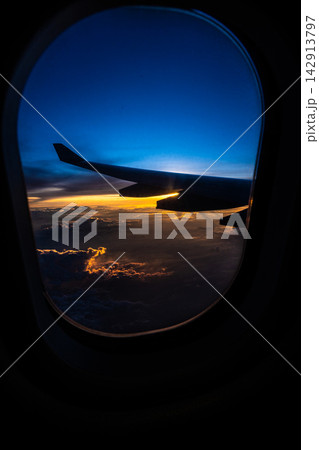 Breathtaking View from an Airplane Window at Sunset, Showcasing Wing Silhouette Against Vibrant Sky Colors and Clouds Below. Breathtaking View from an Airplane Window at Sunset, Showcasing Wing Silhouette Against Vibrant Sky Colors and Clouds Below. 142913797
