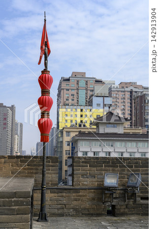 A pole with a red flag on the wall of a 14th-century fortress and modern buildings in Xi'an, China A pole with a red flag on the wall of a 14th-century fortress and modern buildings in Xi'an, China 142913904
