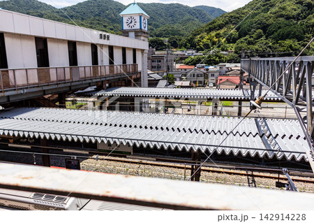 時計台のあるローカル駅のプラットホームと山あいの街並み、高い位置からの俯瞰アングル 142914228