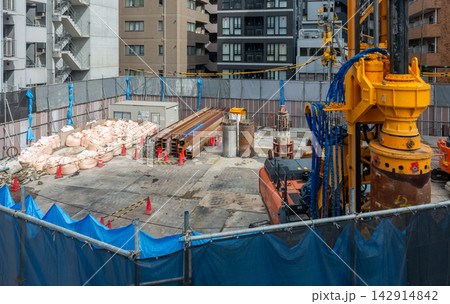 都市部の建設現場の全景 杭打機と資材が並ぶ基礎工事の全景 都市部の建設現場の全景 杭打機と資材が並ぶ基礎工事の全景 142914842