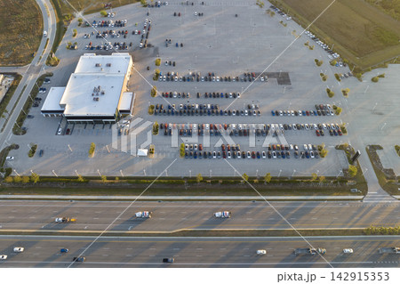 View from above of dealers outdoor parking lot with many brand new cars in stock for sale on highway side. Concept of development of american automotive industry View from above of dealers outdoor parking lot with many brand new cars in stock for sale on highway side. Concept of development of american automotive industry 142915353