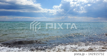coastline of the sea after the storm. small waves and sun with clouds 142915732